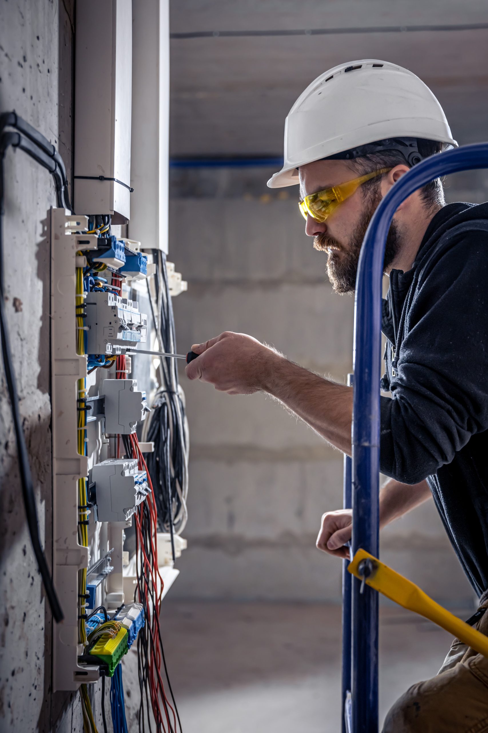 A male electrician works in a switchboard with an electrical connecting cable.